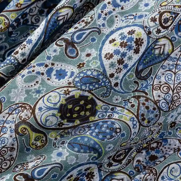 Close-up of Longan Craft Paisley Printed Jersey Fabric By The Yard, 100% cotton with a colorful blue, green, brown, and white paisley pattern featuring floral and geometric details. Slight wrinkles shown on the soft jersey fabric.