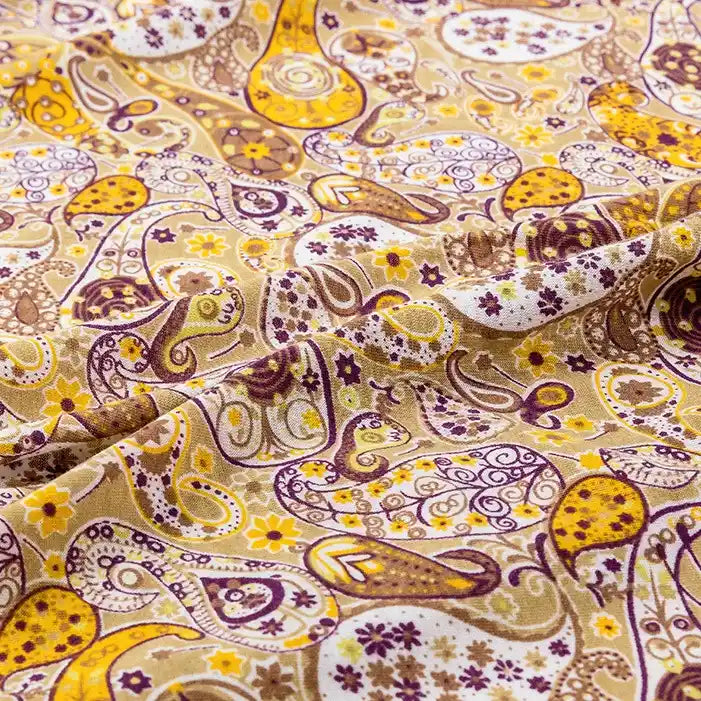 A close-up of Longan Craft's 100% cotton Paisley Printed Jersey Fabric by the yard, showing yellow, brown, and purple paisley designs with small flowers, highlighting the patterned texture ideal for blouses and apparel projects.