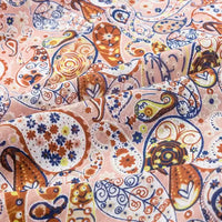 A close-up of Longan Craft's Paisley Printed Jersey Fabric By The Yard shows vibrant orange, blue, and brown floral paisley designs on soft pink 100% cotton jersey, gently folded to highlight its smooth texture—perfect for blouses and apparel.