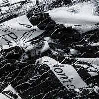 A close-up of Longan Craft’s Floral and Animal Printed 100% Cotton Jersey Fabric, featuring abstract illustrations and partial handwritten text on a slightly wrinkled black and white material—perfect for dresses or jersey clothing.