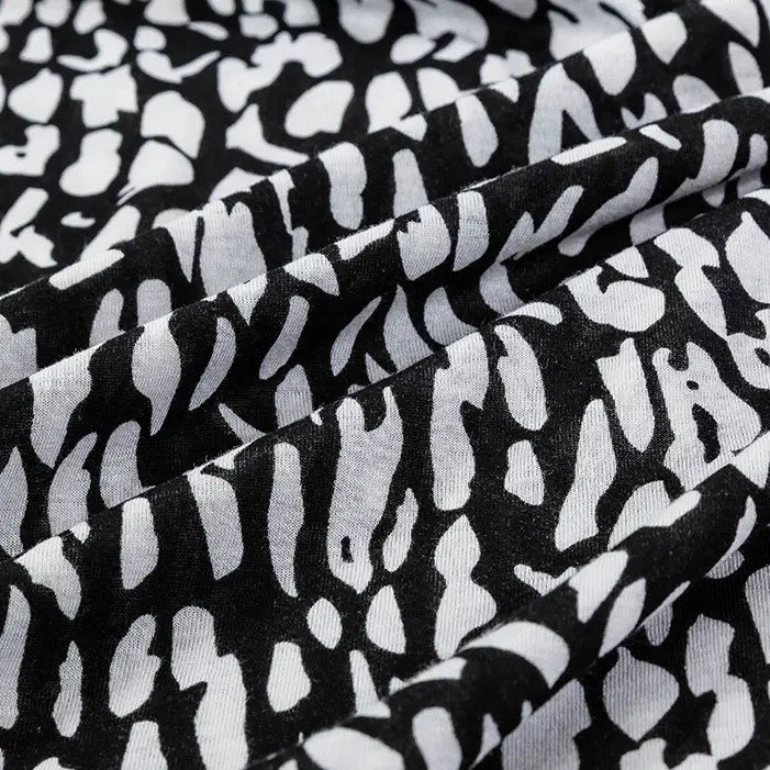 Close-up of Longan Craft's Floral and Animal Printed Jersey Fabric by the yard—100% cotton jersey with a black base, white abstract floral and animal print, and visible gentle folds and texture. Ideal for dresses.