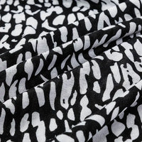 Close-up of Longan Craft's Floral and Animal Printed Jersey Fabric by the yard—100% cotton jersey with a black base, white abstract floral and animal print, and visible gentle folds and texture. Ideal for dresses.