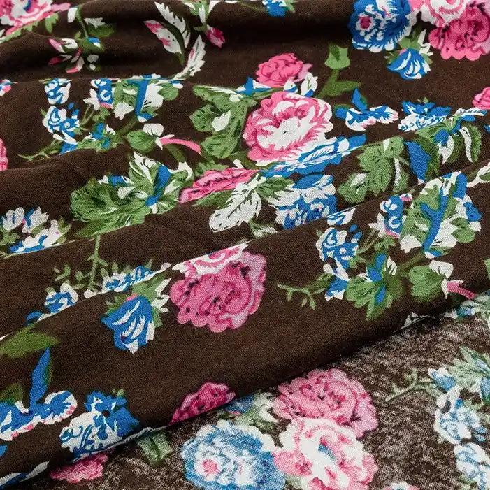 A close-up of Longan Craft's Floral and Animal Printed Jersey Fabric shows 100% cotton with a vibrant print—pink, blue, and white flowers plus green leaves—ideal breathable jersey material for dresses, sold by the yard.
