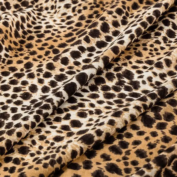 Close-up of Longan Craft Floral and Animal Printed Jersey Fabric, made of 100% cotton. This soft jersey material by the yard features a leopard print in brown, black, and beige—ideal for dresses and clothing projects.