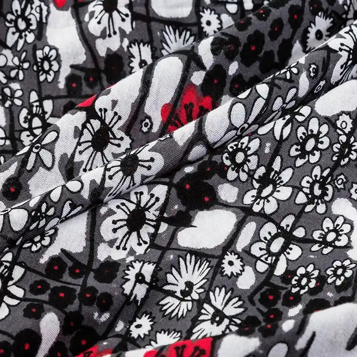 A close-up of Longan Craft’s Floral and Animal Printed 100% Cotton Jersey Fabric shows black, white, and gray floral patterns with red accents. The folded jersey material highlights intricate flower shapes—ideal for dresses by the yard.