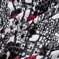A close-up of Longan Craft’s Floral and Animal Printed 100% Cotton Jersey Fabric shows black, white, and gray floral patterns with red accents. The folded jersey material highlights intricate flower shapes—ideal for dresses by the yard.