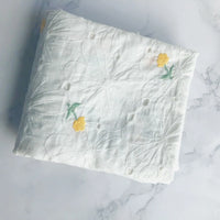 A folded piece of Longan Craft’s Flower Embroidered Cotton Eyelet Fabric by the yard, featuring white cotton eyelet material with floral embroidery, is displayed on a white marble surface.