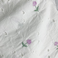 Longan Craft's Flower Embroidered Cotton Eyelet Fabric features white cotton material with large embroidered white flowers and delicate purple blooms with green stems, perfect for dresses and available by the yard.