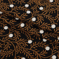 The Flower Embroidered Linen Fabric by Longan craft features black linen with floral embroidery, brown leafy branches, and small white accents. This breathable sewing fabric is ideal for dresses and is sold by the yard.