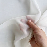 A hand pinches the sheer Georgette Silk Fabric By The Yard from Longan Craft, made of 8 Momme pure mulberry silk crepe, showing the soft, delicate texture and transparency against a plain background.
