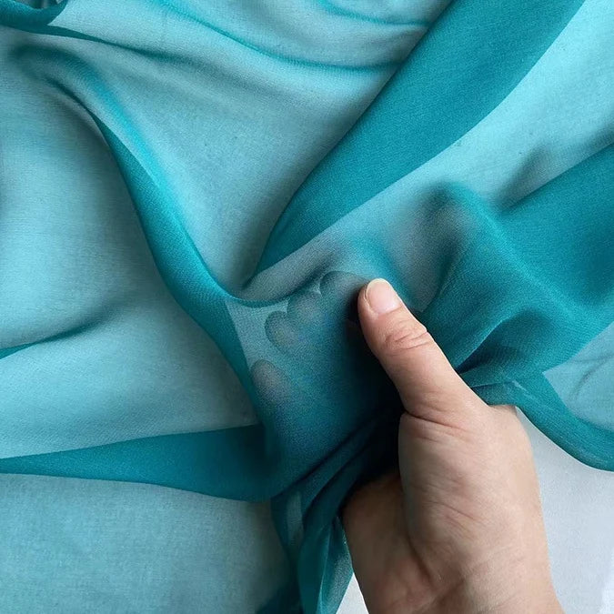 A hand gently gathers Longan Craft's Georgette Silk Fabric by the Yard, made of 8 momme pure mulberry silk crepe, highlighting its delicate, lightweight drape and soft texture against a light background.