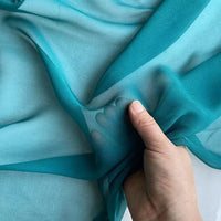 A hand gently gathers Longan Craft's Georgette Silk Fabric by the Yard, made of 8 momme pure mulberry silk crepe, highlighting its delicate, lightweight drape and soft texture against a light background.