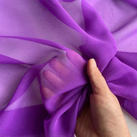 A hand gently grasps Longan Craft's Georgette Silk Fabric By The Yard, made from 8 Momme pure mulberry silk crepe, displaying its sheer, delicate texture and soft drape in the light.