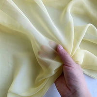 A hand holds and gathers sheer, light yellow Georgette Silk Fabric by Longan Craft, highlighting the 8 Momme pure Mulberry silk crepe’s translucent and delicate texture.