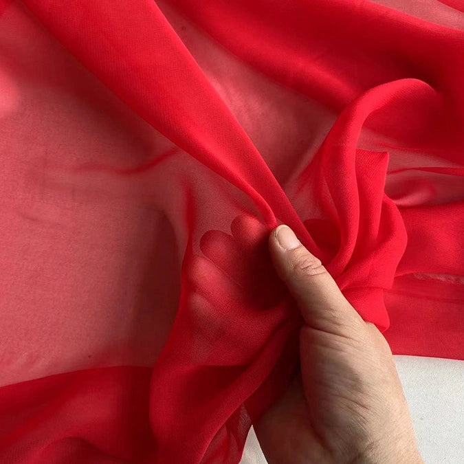 A hand gently holds a piece of Longan Craft Georgette Silk Fabric By The Yard, made from 8 Momme pure mulberry silk crepe, highlighting its lightweight, soft, and translucent texture.