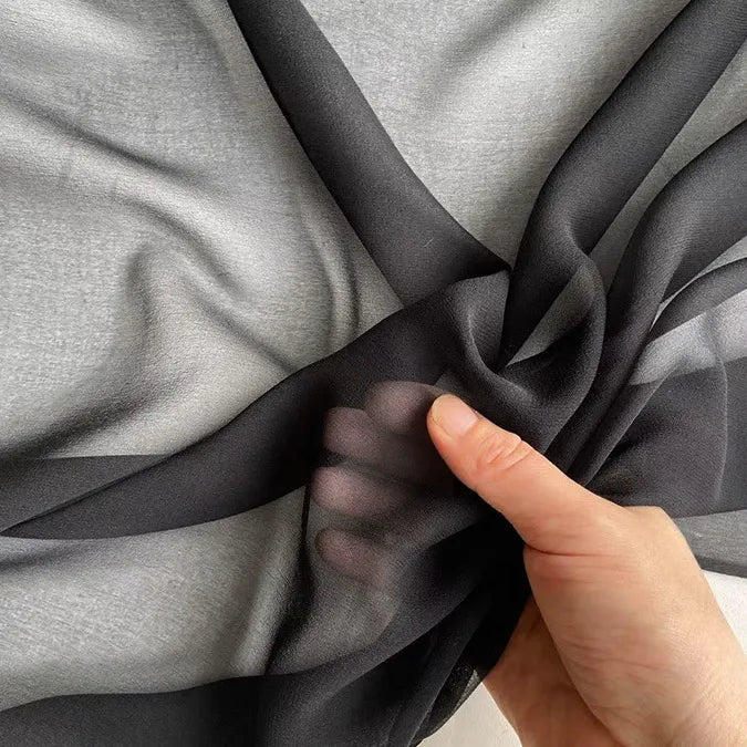 A hand gently gathers Longan Craft's Georgette Silk Fabric By The Yard, showcasing its lightweight, sheer 8 Momme pure mulberry silk crepe texture against a light gray background.