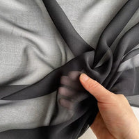 A hand gently gathers Longan Craft's Georgette Silk Fabric By The Yard, showcasing its lightweight, sheer 8 Momme pure mulberry silk crepe texture against a light gray background.