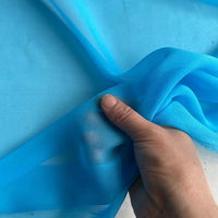 A hand displays Longan Craft's Georgette Silk Fabric By The Yard—8 Momme Pure Mulberry Silk Crepe, highlighting its sheer, lightweight, and translucent texture against a matching blue background.