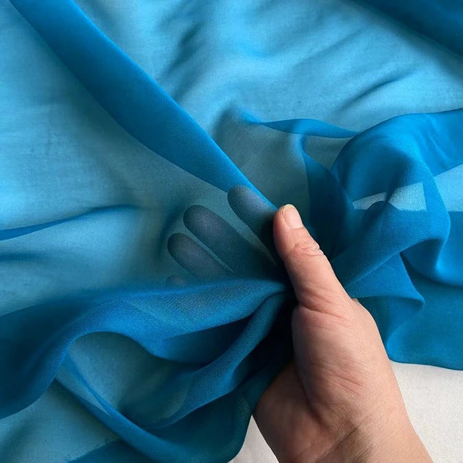 A hand gently lifts Longan Craft’s Georgette Silk Fabric By The Yard—8 Momme Pure Mulberry Silk Crepe—to showcase its transparent, lightweight texture against a light background.