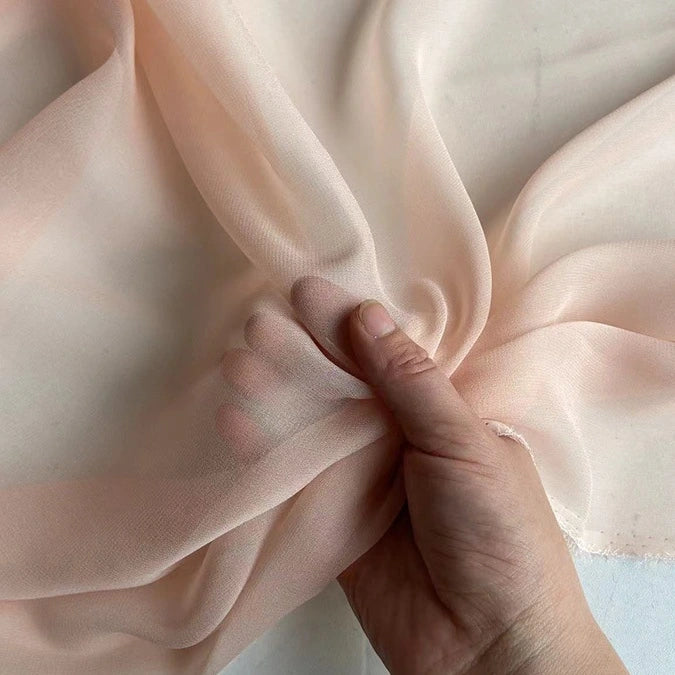 A hand gathers Longan Craft’s Georgette Silk Fabric By The Yard—8 Momme Pure Mulberry Silk Crepe—highlighting its soft, sheer, and translucent texture against a pale background.