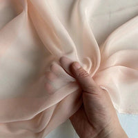 A hand gathers Longan Craft’s Georgette Silk Fabric By The Yard—8 Momme Pure Mulberry Silk Crepe—highlighting its soft, sheer, and translucent texture against a pale background.