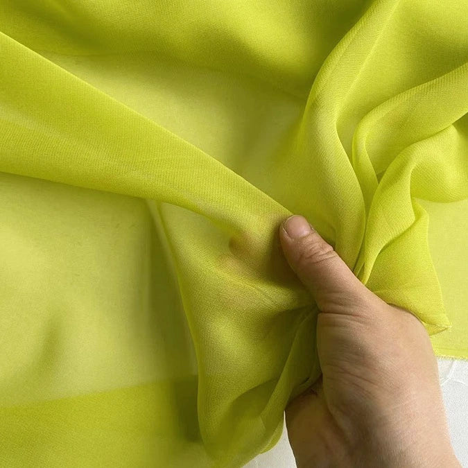 A hand gently pinches the Georgette Silk Fabric By The Yard by Longan Craft, showcasing the sheer, delicate texture of this 8 Momme pure mulberry silk crepe drapery fabric.