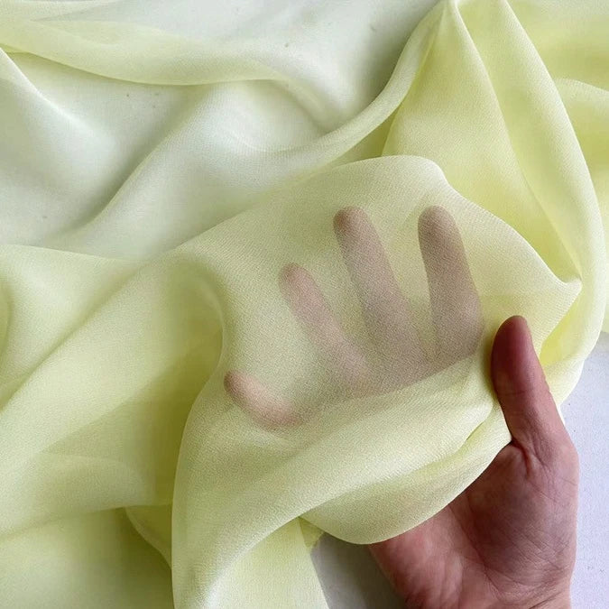 A hand is placed under Longan Craft's Georgette Silk Fabric By The Yard—8 Momme Pure Mulberry Silk Crepe—showing its light yellow, soft, translucent quality and revealing the shape of the hand through the delicate silk drapery.