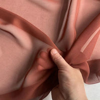 A hand gathers Longan Craft's Georgette Silk Fabric By The Yard—8 Momme Pure Mulberry Silk Crepe—showing its soft, lightweight, and translucent texture against a light background.