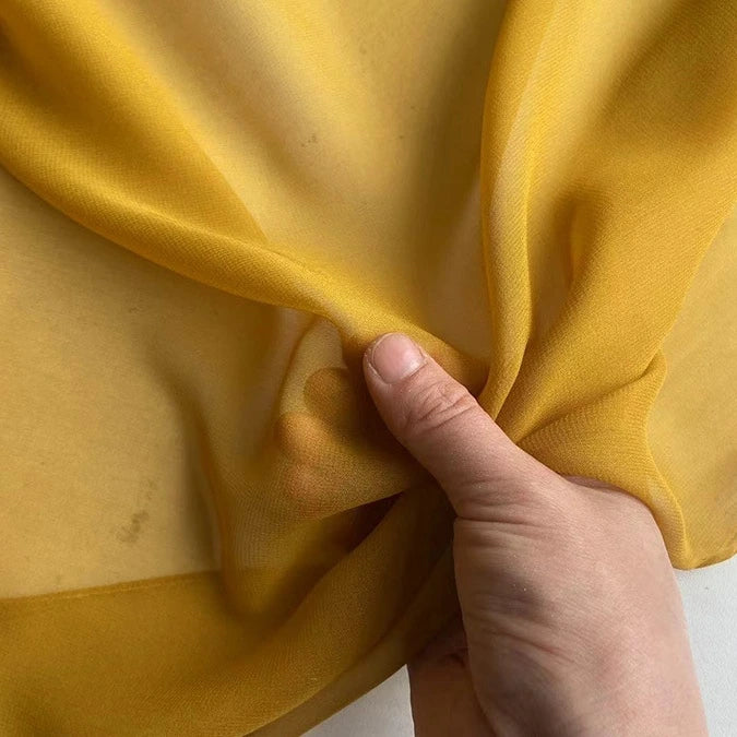 A hand pinches and lifts Longan Craft's Georgette Silk Fabric By The Yard, an 8 Momme pure mulberry silk crepe, showcasing its soft, sheer, and lightweight texture.