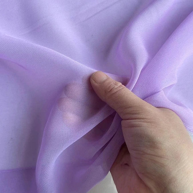 A hand gently holds Longan Craft's Georgette Silk Fabric By The Yard (8 Momme Pure Mulberry Silk Crepe), letting light filter through the soft, sheer material and revealing the outline of fingers beneath its delicate drape.