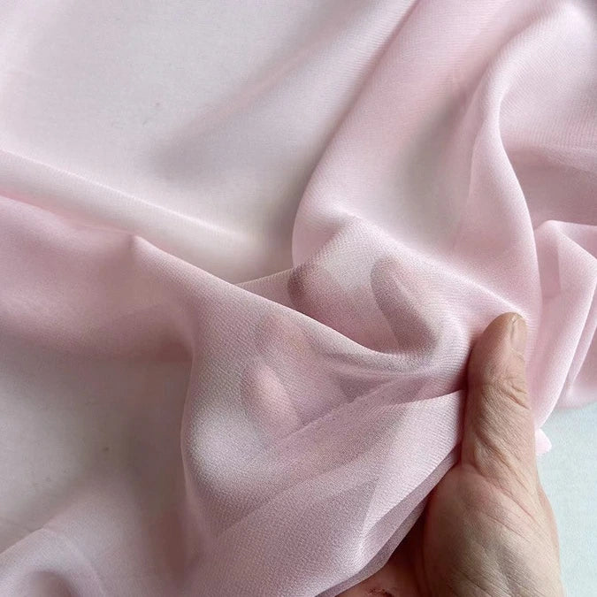 A hand gathers sheer, light pink Georgette Silk Fabric from Longan Craft, highlighting the soft, delicate texture and semi-transparency of this 8 Momme Pure Mulberry Silk Crepe Fabric by the yard—ideal for elegant drapery projects.