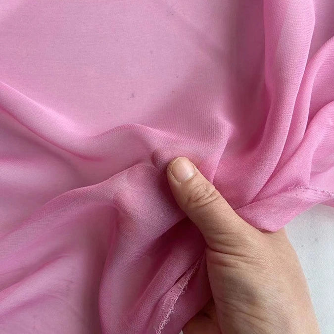 A hand gently holds a piece of Longan Craft’s Georgette Silk Fabric By The Yard, 8 Momme Pure Mulberry Silk Crepe, highlighting its soft, translucent texture against a plain background.