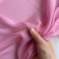 A hand gently holds a piece of Longan Craft’s Georgette Silk Fabric By The Yard, 8 Momme Pure Mulberry Silk Crepe, highlighting its soft, translucent texture against a plain background.