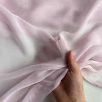 A hand gathers a piece of Longan Craft Georgette Silk Fabric By The Yard, 8 Momme Pure Mulberry Silk Crepe, against a white background, showcasing its delicate, translucent texture and soft drape.