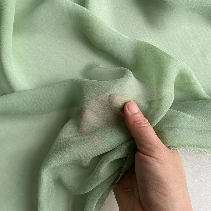 A hand gently holds Longan Craft's Georgette Silk Fabric by the yard—8 momme pure mulberry silk crepe—highlighting its sheer, translucent, and soft drapery texture.