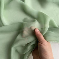 A hand gently holds Longan Craft's Georgette Silk Fabric by the yard—8 momme pure mulberry silk crepe—highlighting its sheer, translucent, and soft drapery texture.