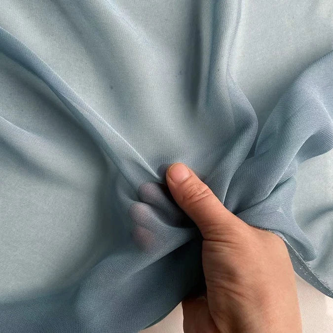 A hand gently holds Longan Craft’s Georgette Silk Fabric By The Yard—8 momme pure mulberry silk crepe—showing its soft, sheer, and delicate texture.