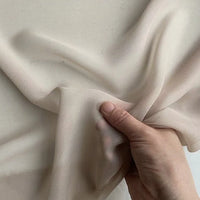 A hand lifts a piece of Longan Craft Georgette Silk Fabric By The Yard—8 Momme Pure Mulberry Silk Crepe—against a neutral background, highlighting its delicate, translucent texture and soft drape.