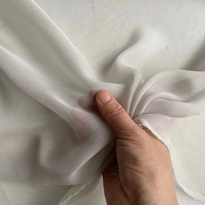 A hand pinches Longan Craft's Georgette Silk Fabric By The Yard—8 Momme Pure Mulberry Silk Crepe—against a neutral background, showcasing the fabric’s soft, sheer, and delicate texture.