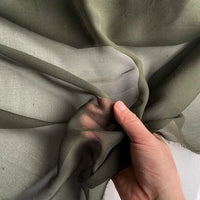 A hand gently grasps Longan Craft's Georgette Silk Fabric by the yard—8 momme pure mulberry silk crepe—showcasing its soft, translucent texture against a light background.