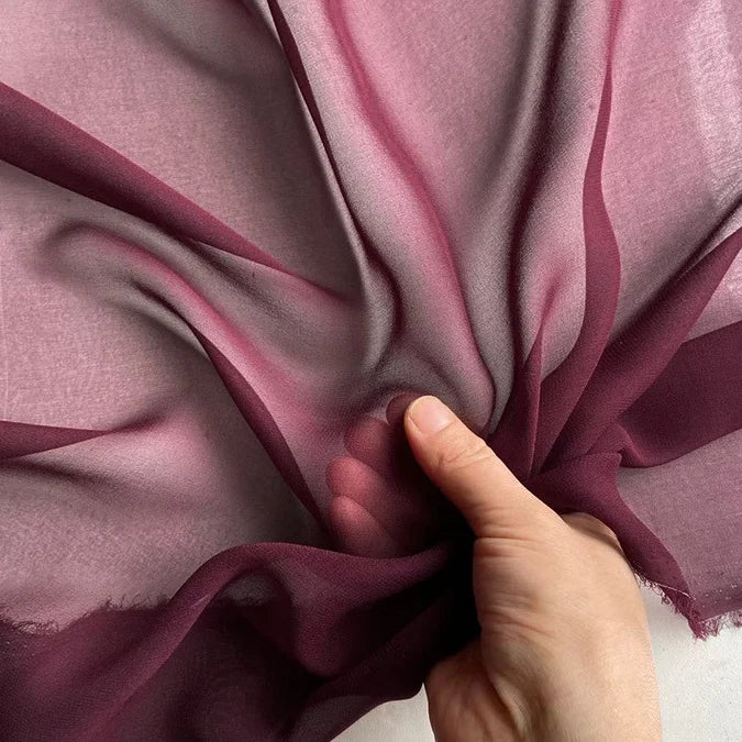 A hand gathers Longan Craft’s Georgette Silk Fabric By The Yard—8 Momme Pure Mulberry Silk Crepe—showing its wine hue, delicate texture, and semi-transparency as light highlights the soft, flowing folds of this drapery fabric.