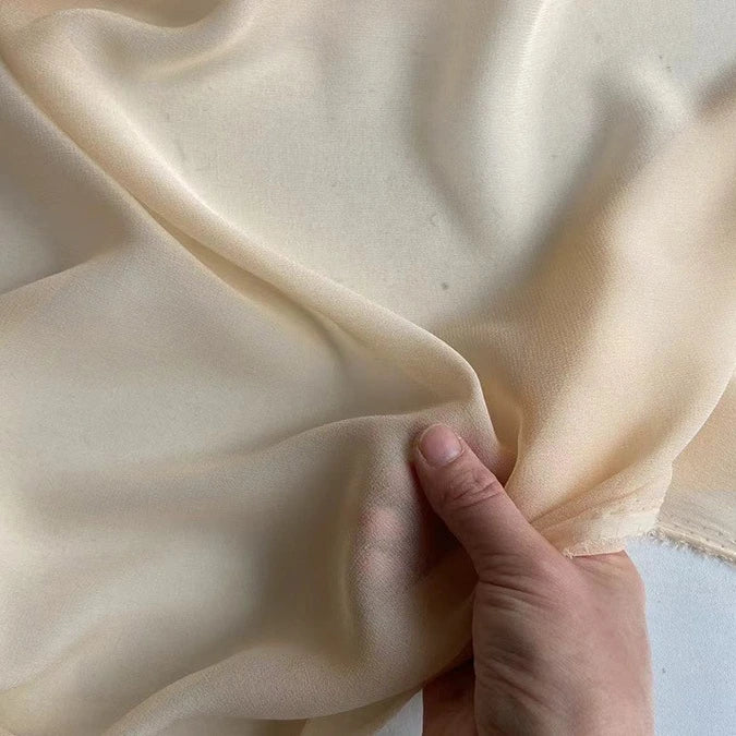 A hand gently lifts a piece of Longan Craft’s Georgette Silk Fabric By The Yard, 8 momme pure mulberry silk crepe, highlighting its delicate, translucent, and soft drape.