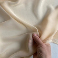 A hand gently lifts a piece of Longan Craft’s Georgette Silk Fabric By The Yard, 8 momme pure mulberry silk crepe, highlighting its delicate, translucent, and soft drape.
