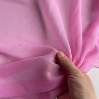 A hand gently gathers sheer, light pink Georgette Silk Fabric by Longan Craft, showcasing the delicate, translucent texture of this 8 Momme pure Mulberry Silk Crepe by the yard.
