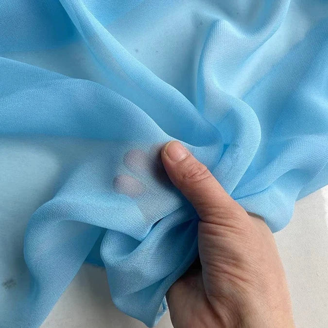 A hand holds and gently gathers Longan Craft's Georgette Silk Fabric By The Yard, made of 8 Momme Pure Mulberry Silk Crepe, highlighting its soft, translucent, and delicate texture—perfect as a silk drapery fabric.