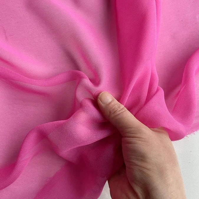 A hand gently bunches Longan Craft's Georgette Silk Fabric By The Yard, made from 8 momme pure Mulberry silk crepe, highlighting its lightweight, soft drape and semi-transparent texture.