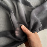 A hand gathers a piece of Longan Craft Georgette Silk Fabric By The Yard—8 Momme Pure Mulberry Silk Crepe—against a light background, highlighting its soft, sheer, and delicate texture.