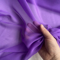 A hand gently holds a piece of Longan Craft Georgette Silk Fabric By The Yard—8 Momme Pure Mulberry Silk Crepe—showing off its sheer, soft drape as light passes through and reveals the fingers beneath.