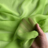 A hand gently holds Longan Craft's Georgette Silk Fabric By The Yard—8 momme pure mulberry silk crepe, sheer and light green, its semi-transparent quality lets fingers show through the soft drapery.