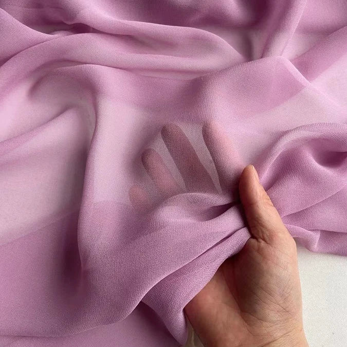 A hand gently grasps Longan Craft's Georgette Silk Fabric By The Yard—8 Momme pure mulberry silk crepe—showing fingers through the soft, sheer, light purple material.